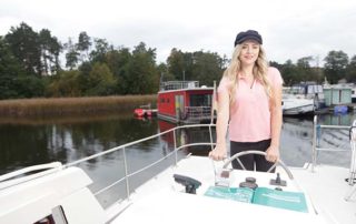 Junge Frau am Steuer eines gemieteten Hausbootes in der Mecklenburgischen Seenplatte.