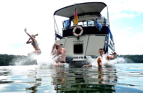 Freunde springen gemeinsam von Bord eines Hausbootes ins Wasser