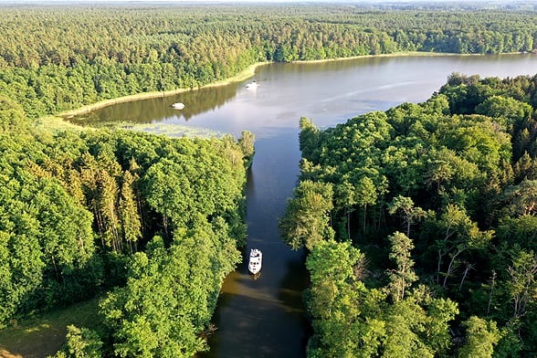 Das Hausboot Revier in der Mecklenburgische Seenplatte in Brandenburg und Mecklenburg ist ein Eldorado für Hausboote. Seen und Flüsse reihen sich aneinader. Wie hier in der Kleinseenplatte wo ein Boot von einem See zum anderen durch einen Kanal, umgeben von dichtem Wald, fährt.